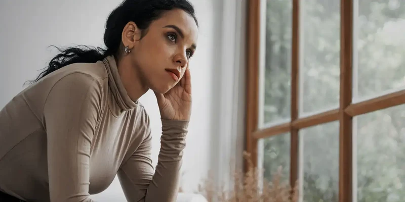 kembali mental health woman sitting couch looking out window