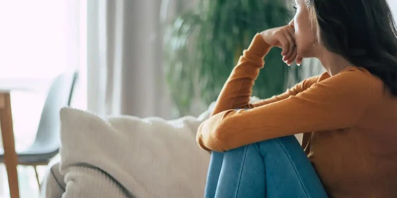 kembali mental health woman sitting couch looking out window