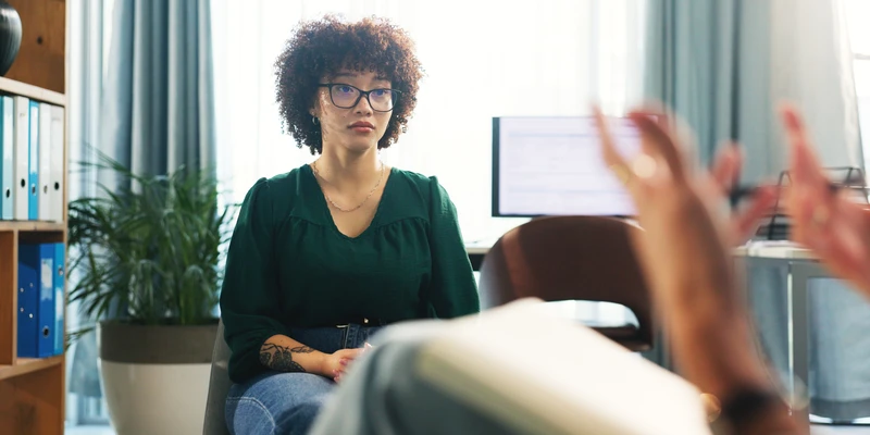 kembali therapy woman glasses sits desk hands raised